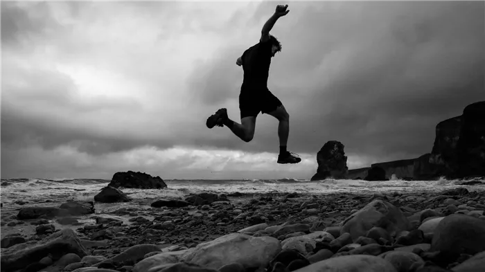 A low-angle shot shows a man in the air as he runs on a rocky beach.